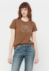 T-shirt en coton marron avec un design décoratif de perles et de sequins élaborés sur la poitrine, complété par des manches courtes simples.