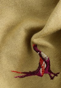 Brede gebreide stof in beige met een gestructureerde afwerking, voorzien van meerkleurige borduursels van een vogel in rode, oranje en paarse tinten aan de zijkant.