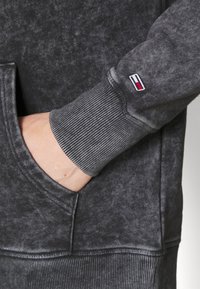 Felpa grigia scura con una finitura testurizzata, caratterizzata da un polsino a coste, una tasca frontale e una piccola etichetta logo interna.