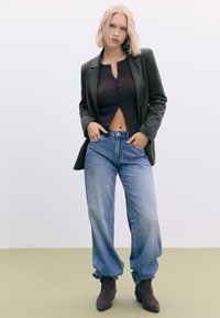 Mørkegrøn blazer, ribbet brun crop top, lys blå løse jeans og brune ankelstøvler. Lige snit, blød tekstur og afslappet pasform.