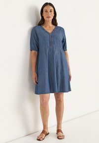Denim jurk met korte pofmouwen, V-hals en decoratieve stiksels langs de voorkant. Kleur is middelblauw met een losse pasvorm.