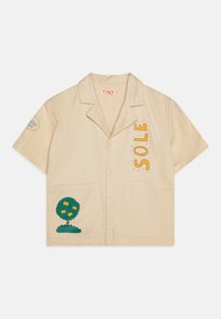 Camicia beige a maniche corte con ricamo di un albero, testo arancione che legge "SOLE", due tasche frontali e un design del colletto classico.