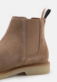 Brązowy zamszowy botek za kostkę z teksturowanymi elastycznymi panelami bocznymi, przeszywaniem, gumową podeszwą i pętelką na obcasie z kolorowymi akcentami.