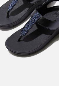 Zwarte teenslippers hebben een gestructureerde zool, een slank ontwerp en een band versierd met blauwe en doorzichtige strass-steentjes voor extra detail.