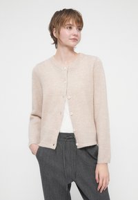 Cárdigan de un beige claro, hecho de material suave, con cuello redondo, mangas largas y pequeños botones en la parte delantera.