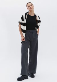 Cardigan de rayas negro y blanco de punto sobre una camiseta de tirantes negra, combinado con pantalones grises holgados y botines negros de tacón grueso.