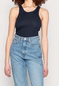 Top a coste blu navy con spalline larghe, abbinato a jeans di colore azzurro chiaro a vita alta con chiusura a bottone e texture in denim classico.