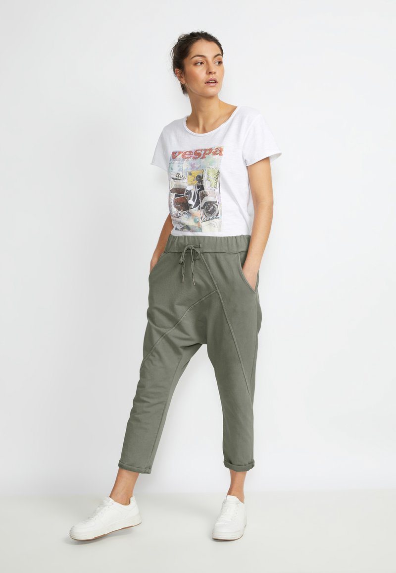 T-shirt graphique blanc avec impression "vespa" ; joggers cintrés vert olive avec taille élastique et poches latérales ; associés à des baskets blanches.
