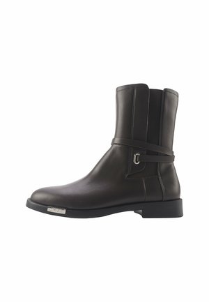Schwarze Lederknöchelschuh mit glatter Oberfläche, Riemendetail um den Knöchel und quadratförmiger Spitze. Verfügt über einen niedrigen Blockabsatz und ein Metall-Logoprinzip.