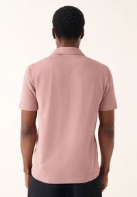 Polo a maniche corte in tessuto rosa chiaro, con colletto classico e una texture liscia, con orlo dritto sul fondo.