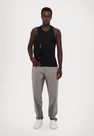 Melnā beznogaklā tanka blūze, pelēkas sporta bikses ar acs detaļām un baltas kedas; pozē ar melnu krustu somu uz pleca.