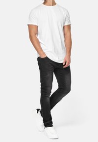 Witte katoenen T-shirt met korte mouwen, gecombineerd met slim-fit zwarte jeans en witte sneakers, die een casual, moderne stijl laat zien.
