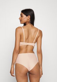 Núdová bezšvová lingerie súprava pozostávajúca z jemnej látkovej braletky s nastaviteľnými ramienkami a zodpovedajúcich vysokých nohavičiek, obe v minimalistickom dizajne.