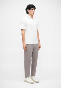 Tricou polo alb cu guler negru, pantaloni de trening gri și adidași albi. Polo-ul are un mic logo pe piept.