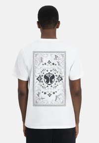Witte T-shirt met korte mouwen, voorzien van een gedetailleerd zwart-wit bloemenmotief met vlinders en een centraal embleem op de achterkant.