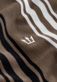 Textil hullámzó csíkos mintával, barna, krémszín és fekete árnyalatokban, fehér hímzett korona logóval. Puha textúra.