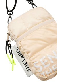 Päuffy beiger Umhängetasche mit schwarzem Zubehör, ausgestattet mit einer Fronttasche, einem kontrastierenden Logo und neon-gelben Akzenten an den Zipper-Ziehen.