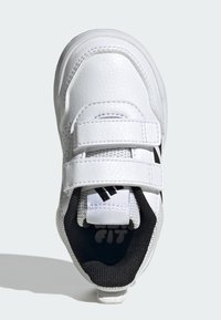 Bijela sintetička tenisica s dva Velcro remena, teksturiranim gornjim dijelom i crnim unutarnjim postavom. Na jezičku se nalazi detalj s logotipom, a prednji dio je zaobljen.