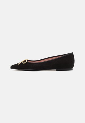 Black suede flat shoe with a pointed toe, featuring a gold metal accent in the shape of a bow and a smooth inner lining.