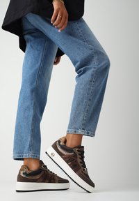 Bruine en zwarte sneakers met een gestructureerd ontwerp, witte plateauzool en dierenprintaccenten. Gecombineerd met lichtblauwe jeans.