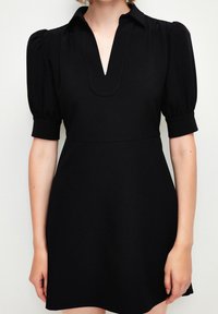 Vestido corto negro con cuello en V, mangas abullonadas y tejido texturizado, que enfatiza una cintura ajustada y una falda acampanada.