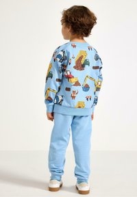 Lichtblauwe trui met kleurrijke bouwvoertuigenprints en bijpassende blauwe joggingbroek. De stof lijkt zacht met geribbelde manchetten.