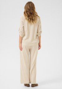 Krémovo-beige pruhovaný top a široké nohavice, ktoré majú voľný strih, rolované rukávy a mäkkú textúrovanú tkaninu. Hnedé členkové čižmy.