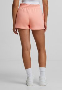 Rosa sweatshorts med elastisk midja, slät textur och avslappnad passform. Matchat med vita sneakers och strumpor.
