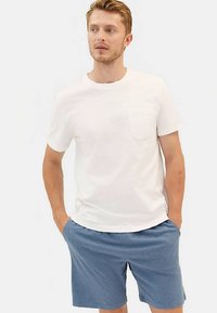 Vit bomulls-t-shirt med vänster bröstficka, kombinerad med ljusblåa shorts i mjuk textur, med elastisk midjeband och avslappnad passform.