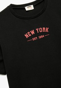Czarny bawełniany t-shirt z krótkim rękawem, z czerwoną grafiką "NEW YORK EST. 1984" w zakrzywionym kształcie z przodu. Okrągły dekolt.