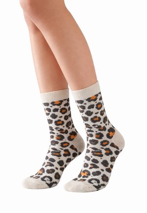 Beine mit knielangen Socken mit beigem Hintergrund und schwarzem, orangefarbenem Leopardenmuster vor weißem Hintergrund.