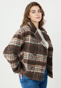 Veste en mélange de laine écossaise marron à col cranté, double boutonnage, avec des motifs contrastés crème et orange. Caractérisée par une coupe décontractée et des poches latérales.