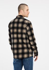 Camisa de franela a cuadros en negro y marrón con cuello, mangas largas y un corte relajado, combinada con jeans de mezclilla azul.