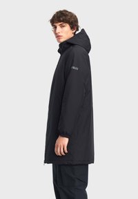 Parka a cappuccio nero con una vestibilità rilassata, dotata di polsini elasticizzati e zip frontale. Logo sulla manica sinistra. Tessuto liscio e resistente all'acqua.