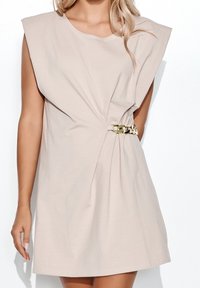 Beiges Kleid mit kurzen Ärmeln, gedrehter Vorderseite und einem goldenen Kettenakzent an der Taille. Hergestellt aus weichem, leichtem Stoff.
