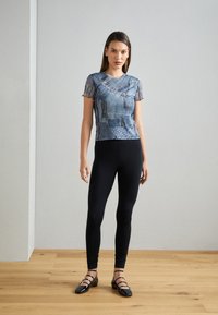 Camisa gráfica de denim azul con mangas cortas y con volantes; combinada con leggins negros y bailarinas negras con detalles de hebilla. Fondo liso.