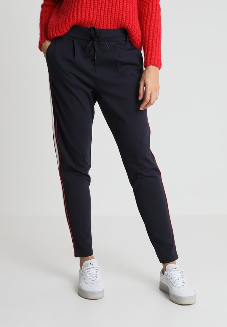 Pantalon de survêtement bleu marine avec des bandes latérales rouges, taille élastique avec cordon de serrage, coupe fuselée, associé à des baskets blanches.