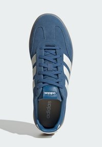 Plave antilop tenisice s bijelim dizajnom u obliku tri pruge, okrugli vrh i ravne vezice. Imaju podstavljeni ovratnik i teksturiranu gumenu vanjsku površinu.