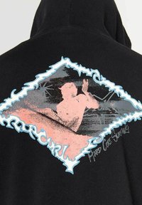 Haut à capuche noir présentant un graphique en forme de diamant bleu et rose, montrant une personne surfant sur un fond texturé.