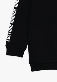 Felpa nera con maniche lunghe e testo "CULTURE MAKER" in grassetto bianco sulla manica sinistra e polsini a coste. Texture morbida.