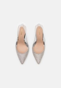 Spetsiga klackskor med en metallisk silverfärgad textur, klara sidor och en nude innersula. Har en stilren design med minimala accenter.