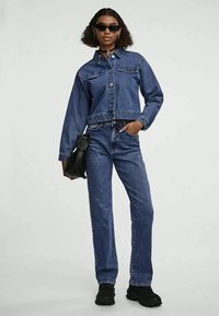 Jeans jakna i traperice u tamnoplavoj boji. Jakna ima dvije prednje džepove i skraćeni dizajn. Crne sunčane naočale i mala crna torba upotpunjuju izgled.