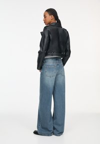 Zwart leren cropped jack met een gelapte kraag en ritsdetails, gecombineerd met lichtblauwe wijde denim jeans met achterzakken.