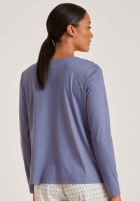 Lange mouwen top in lichtpaarse stof met een ronde hals en een relaxte fit, gecombineerd met gestreepte gele en blauwe broek.
