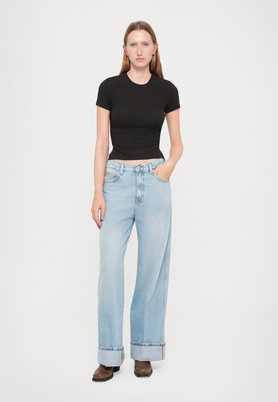 Black fitted short-sleeve top paired with light blue wide-leg jeans with rolled cuffs and brown ankle boots. Neutral background.