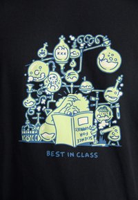 Sort t-shirt med et tegneserie-design i lys grøn og blå, der viser en figur, der læser en bog blandt videnskabsrelaterede grafik og tekst.