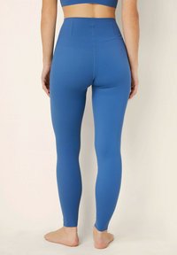 Hoge blauwe leggings gemaakt van rekbaar materiaal, met een gladde textuur en een aansluitend ontwerp. Blote voeten zichtbaar.