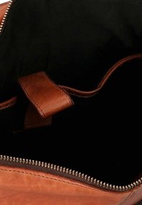 Interno di una borsa a mano in pelle marrone con una superficie liscia, dotata di una chiusura con zip e di una tracolla in pelle. Fodera in tessuto scuro visibile all'interno.