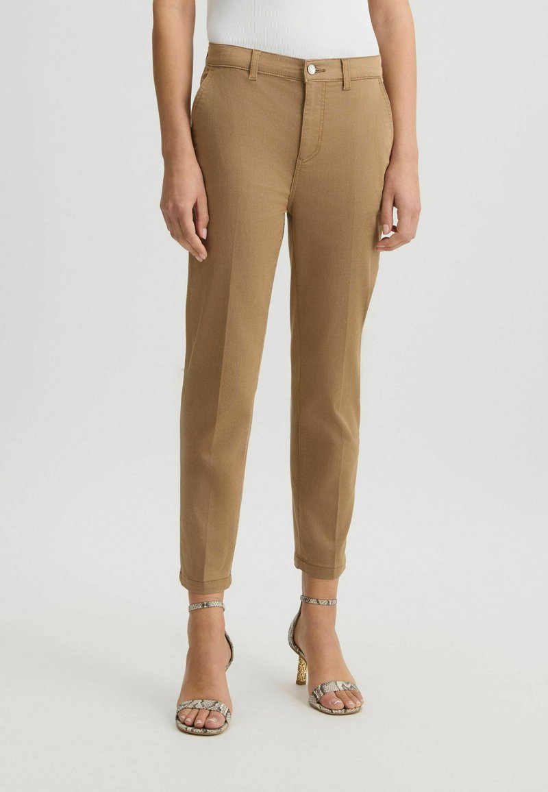 Pantalons marron fuselés en tissu texturé, dotés d'une fermeture à l'avant et de poches latérales, associés à des talons à lanières à motifs.