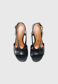 Mustat nahkaiset slingback-sandaalit avoimella varpaalla, joissa on leikattuja sivuja ja pieni nilkkaremmissä solki. Ruskea sisäpohja näkyvissä.